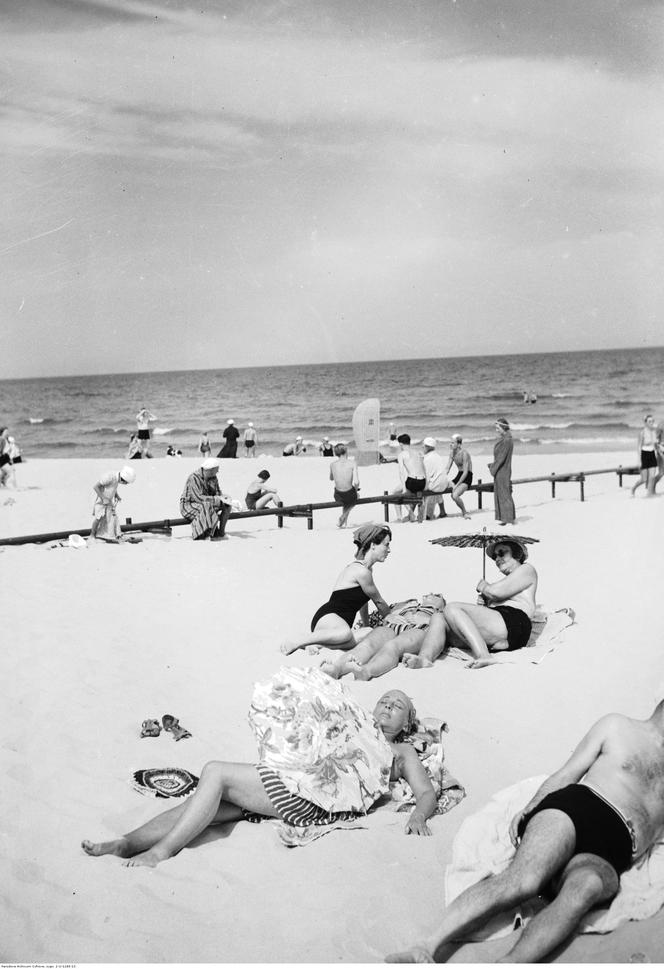 Plażowicze podczas wypoczynku nad morzem Bałtyckim. W tle port. Zdjęcie zrobiono w Gdyni pomiędzy 1923-1935 rokiem