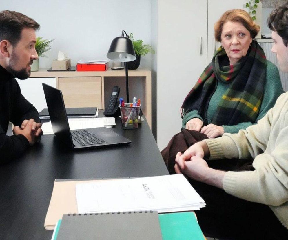 Łukasz, Józefina i Cezary siedzą przy biurku z laptopem, prawdopodobnie podczas rozmowy dotyczącej zarekwirowanych klejnotów Rawiczowej. Józefina ma na sobie zielony sweter i kraciasty szal, wyraża zmartwienie, co wskazuje na emocjonalny kontekst fabuły Barw szczęścia, o której przeczytasz więcej na Super Seriale.