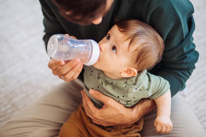 dziecko pijące wodę z butelki podawanej mu przez ojca