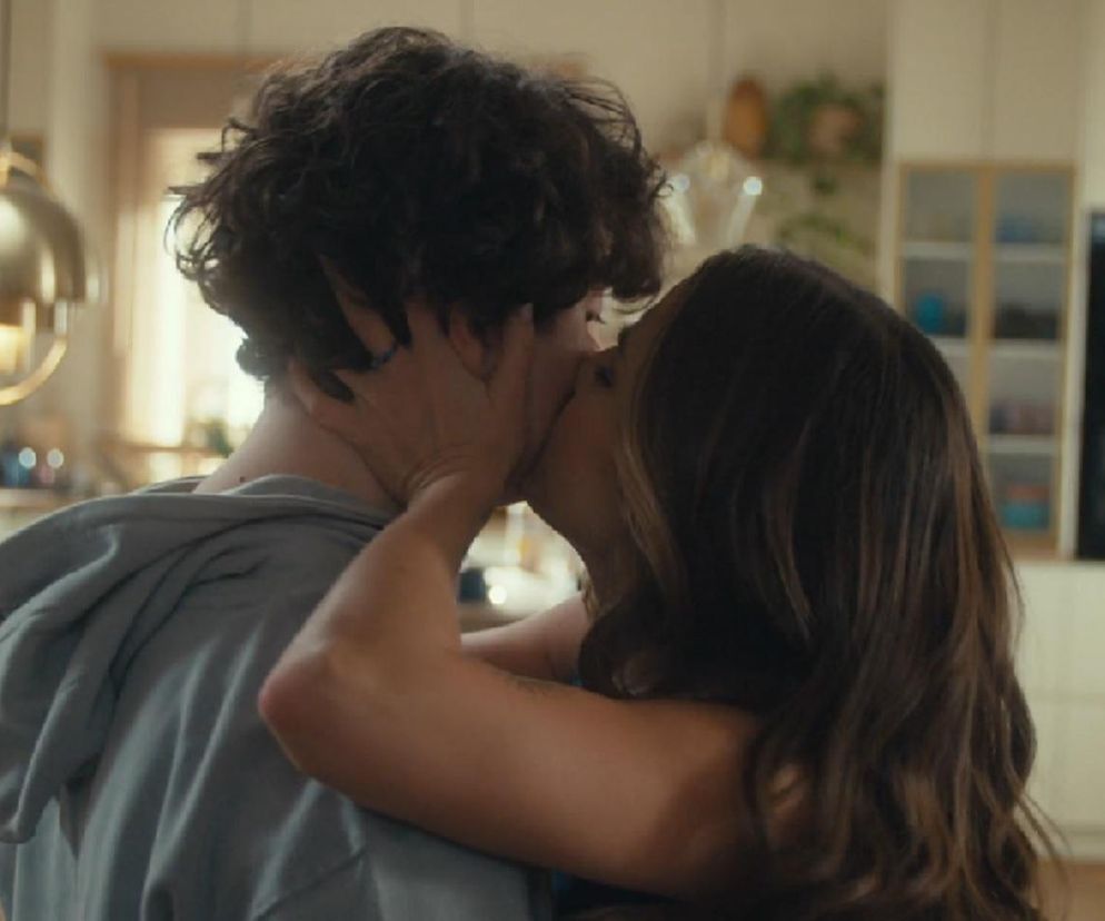 Kacper Boski i Paula (Julia Wieniawa) w intymnym pocałunku w kuchni, scena z serialu Rodzinka.pl, podkreślająca ich skomplikowaną relację. Więcej o ich losach znajdziesz na stronie Super Seriale.