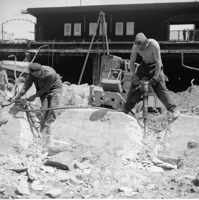 Robotnicy z młotami pneumatycznymi kruszą betonowe elementy. 
