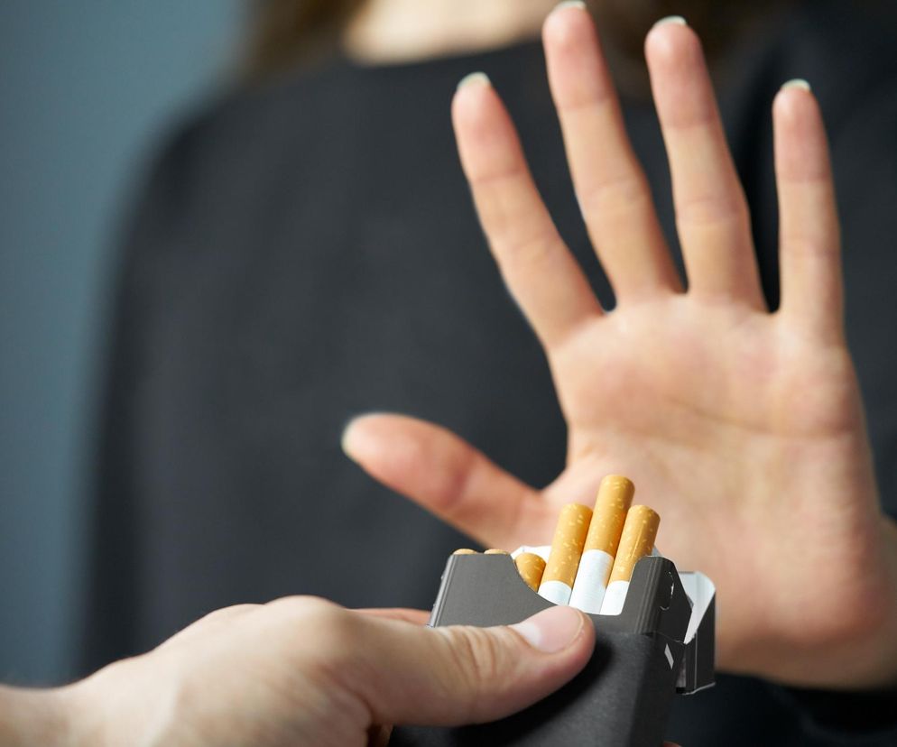 Osoba odmawia przyjęcia papierosów, wykonując gest stop dłonią, co symbolizuje rzucenie palenia i troskę o zdrowie mózgu. Na tle widać drugą dłoń oferującą paczkę papierosów. Na portalu Poradnik Zdrowie znajdziesz więcej informacji o tym, jak zerwanie z nałogiem chroni przed demencją.
