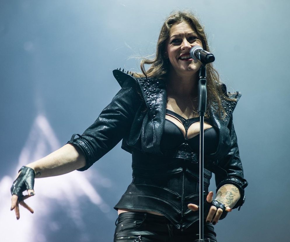 Floor Jansen podczas solowego występu, ubrana w czarną, skórzaną stylizację z gorsetem i krótką kurtką z ćwiekami, śpiewa do mikrofonu, z uśmiechem i uniesioną lewą dłonią w rękawiczce bez palców. Więcej o jej koncercie na naszym portalu.
