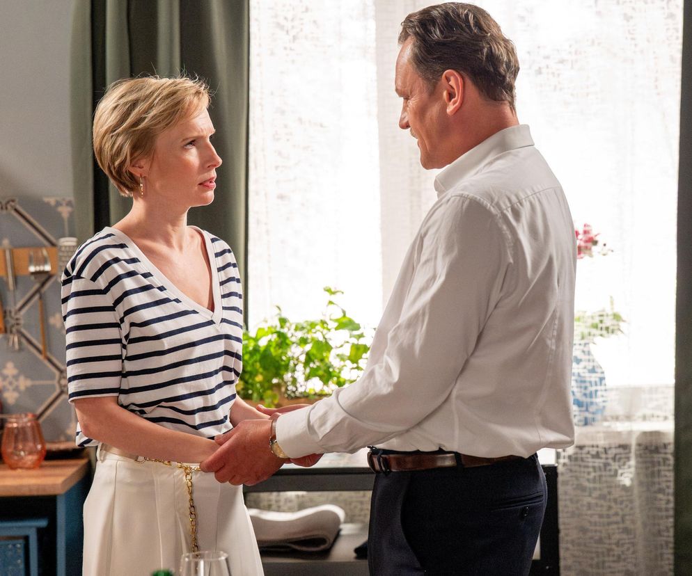 Sonia (Weronika Nockowska) w bluzce w paski i białej spódnicy, trzymająca dłonie Stefaniaka (Paweł Ławrynowicz) w białej koszuli, w mieszkaniu. Scena z serialu Barwy szczęścia, której szczegóły można znaleźć na Super Seriale.