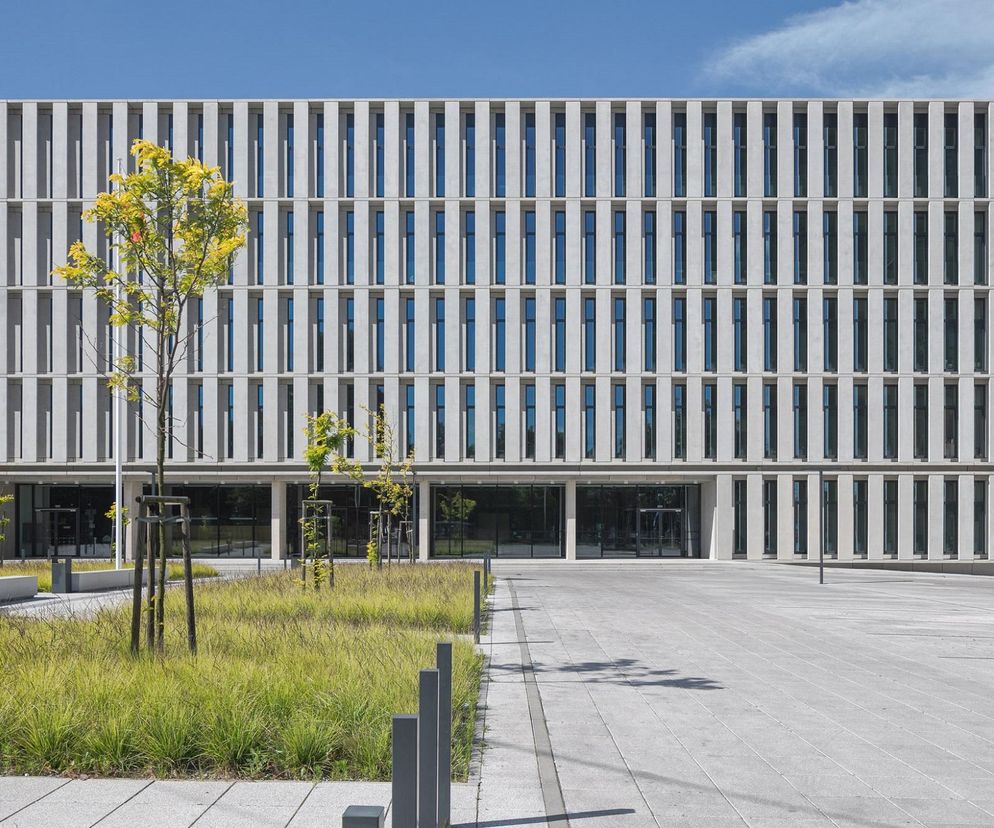 Elegancka, nowoczesna bryła Sądu Rejonowego w Częstochowie, zaprojektowana przez heinlewischer, z prostymi, wertykalnymi panelami na elewacji. Przed budynkiem betonowy plac z trawnikami i młodymi drzewami. Więcej o architekturze tego typu przeczytasz na Architektura Murator Plus.