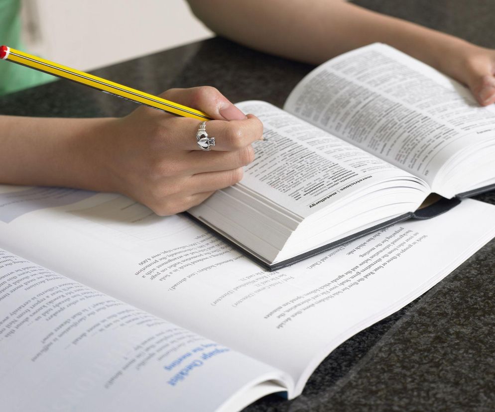 Osoba w zielonej koszulce siedząca przy biurku, trzymająca w dłoni ołówek z gumką i notująca w otwartej książce, obok leży inna otwarta książka. To stock photo ilustrujące sposoby na odmłodzenie mózgu, o których przeczytasz na Poradnik Zdrowie.