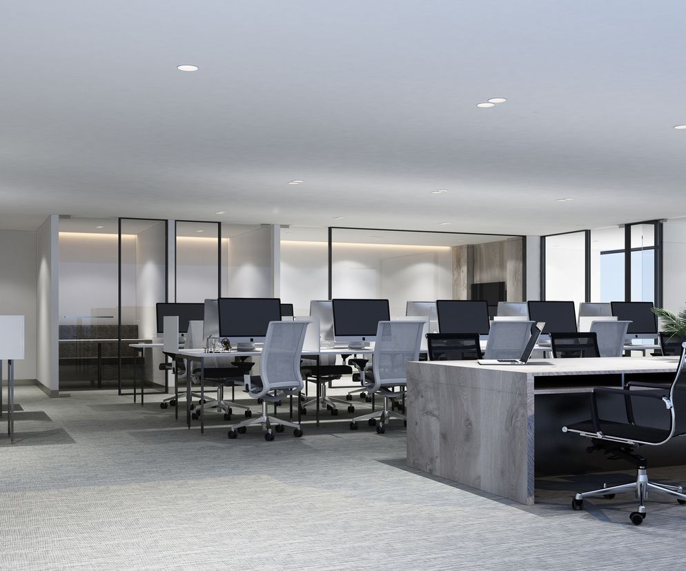 Nowoczesne biuro w stylu open space z wieloma pustymi stanowiskami pracy, krzesłami obrotowymi, komputerami i biurkami. Zdjęcie ilustruje wyzwania związane z higieną i rozprzestrzenianiem się zarazków w miejscu pracy po pandemii, o czym przeczytasz na Poradnik Zdrowie.