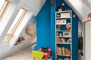 Aneks do zabawy jest spory. Ścianę kominową z tej strony pomalowano na niebiesko. Dzięki temu tak jak kolorowe mebelki ożywia wystrój. W obu skosach zamontowano okna dachowe – dwa duże po jednej stronie i dwa mniejsze po drugiej. Rolety sterowane pilotem
