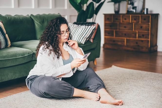 Kobieta plus size siedzi na dywanie z telefonem w ręku