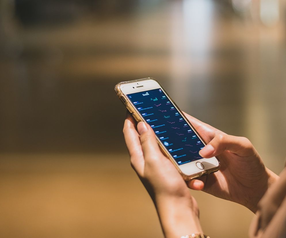 Bliska perspektywa rąk trzymających smartfon z wyświetloną aplikacją finansową, pokazującą wykresy i dane rynkowe. Obraz nawiązuje do ekspansji Revoluta i jego oferty, o której przeczytasz więcej na Super Biznes.