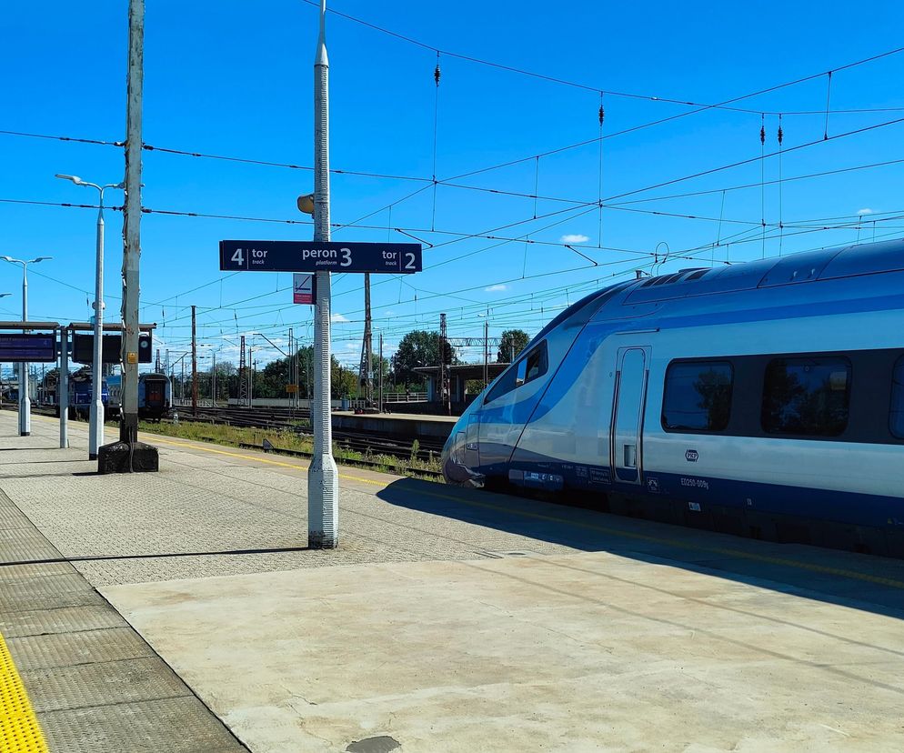 Nowoczesny pociąg Pendolino PKP Intercity na dworcu, gotowy do odjazdu. Zdjęcie ilustruje rozwój Kolei Dużych Prędkości w Polsce, o czym przeczytasz więcej na portalu Super Biznes. Scena przedstawia peron z tablicami informacyjnymi, niebo jest bezchmurne.