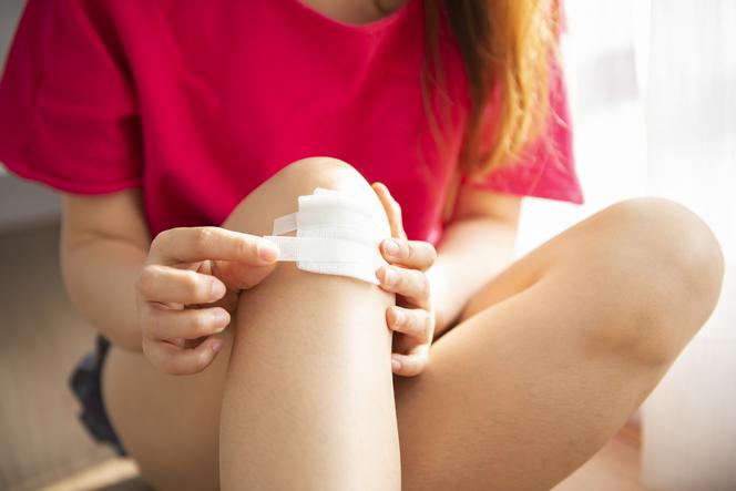 Kobieta nakleja plaster na skaleczone kolano