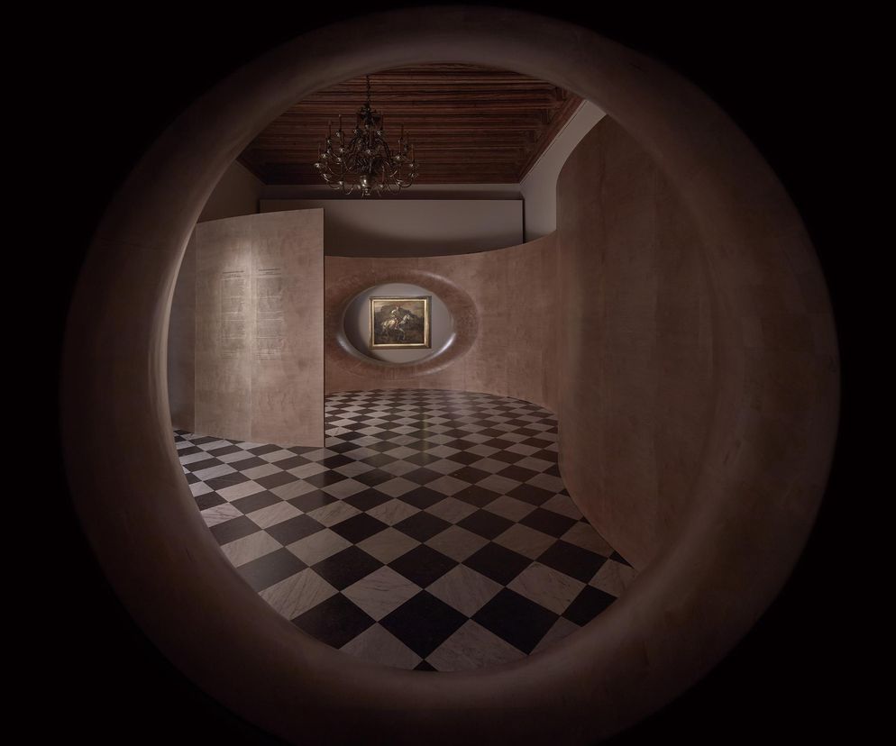 Nowoczesna instalacja architektoniczna ekspozycji „Królewski Rembrandt na Wawelu” projektu NArchitekTURA w Krakowie. Centralnie umieszczony obraz „Jeździec polski” w owalnym otworze, na tle ściany ze sklejki. Czarno-biała szachownica na posadzce z marmuru. Więcej o architekturze wnętrz na Architektura Murator Plus.