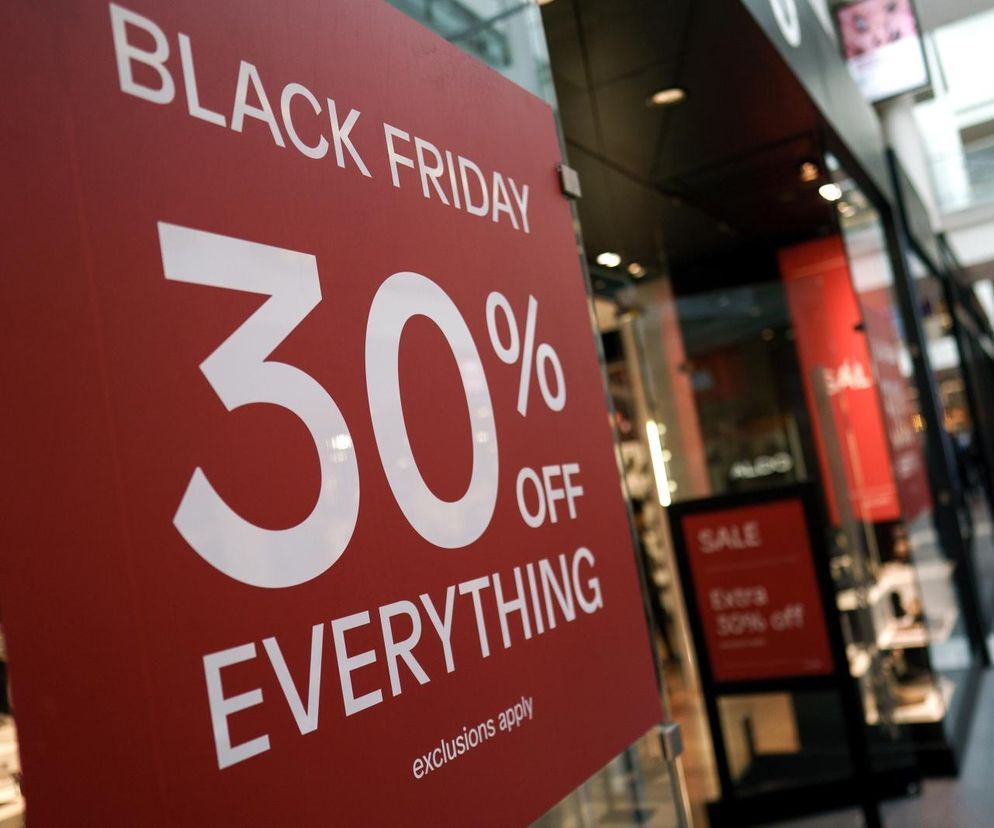 Czerwona tablica z napisem Black Friday 30% OFF EVERYTHING przed sklepem, symbolizująca gorączkę wyprzedaży. W tle widać wejście do centrum handlowego z innymi promocjami. Dowiedz się, jak mądrze kupować sprzęt AGD w Black Friday, czytając artykuł na Super Biznes.
