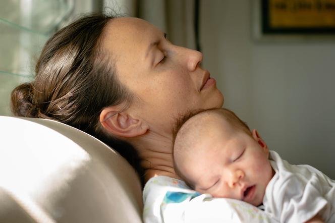 Kobieta z noworodkiem odpoczywa z zamkniętymi oczami