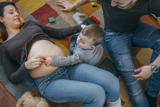 kobieta w ciąży i jej mąż bawią się z dzieckiem na podłodze 