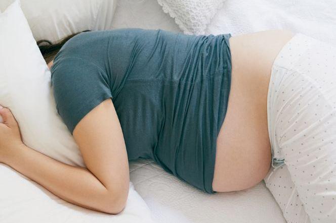 Zdenerwowana kobieta w ciąży leżąca na łóżku  i zakrywająca głowę poduszką
