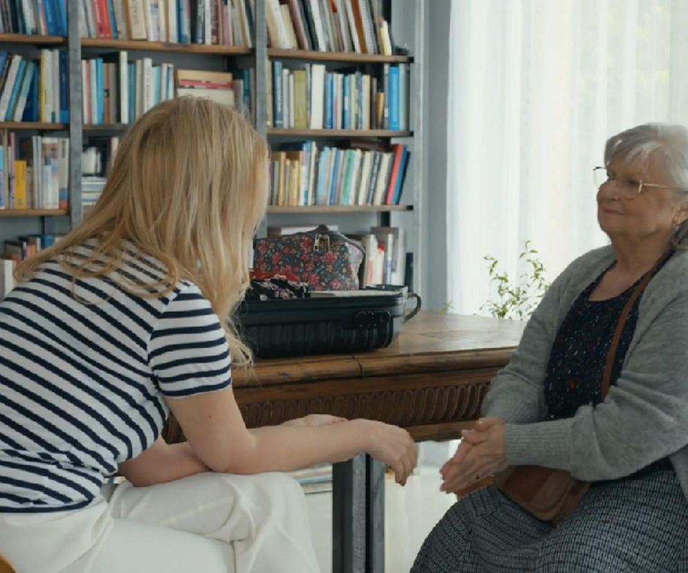 Karolina (Marta Dąbrowska) rozmawia z Amelią (Stanisława Celińska) w bibliotece. Karolina, ubrana w biało-granatową bluzkę w paski i białe spodnie, siedzi na krześle, słuchając starszej kobiety. Amelia w szarym swetrze i okularach zapewnia ją o miłości Bruna, co można przeczytać na Super Seriale.