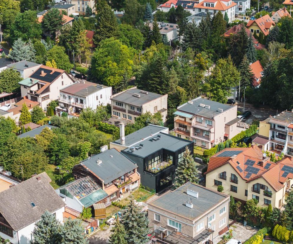 Widok z lotu ptaka na Casafutura, czyli nowoczesny dom modułowy z ciemną elewacją i dużymi oknami, w otoczeniu zielonych drzew i tradycyjnych budynków na wrocławskim Biskupinie. Projekt Rewizja grupa projektowa prezentowany na Architektura Murator Plus.