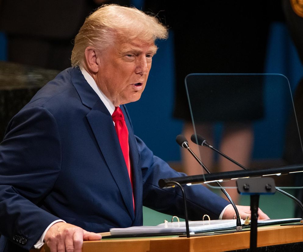 Były prezydent USA Donald Trump w granatowym garniturze i czerwonym krawacie przemawia na konferencji, co widać na Super Biznes, gdzie analizuje się jego wpływ na rynki finansowe. Widoczne mikrofony i materiały na pulpicie.