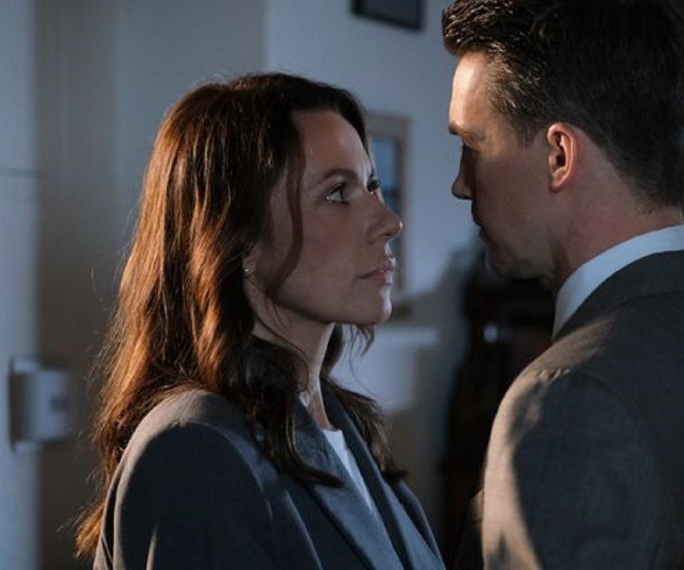 Martyna (Magdalena Turczeniewicz) i Jakub (Krzysztof Kwiatkowski) z serialu M jak miłość patrzą sobie w oczy w pomieszczeniu. Kobieta ma długie, falowane włosy i szarą marynarkę, a mężczyzna jest ubrany w garnitur i białą koszulę. Więcej o ich losach dowiesz się na Super Seriale.