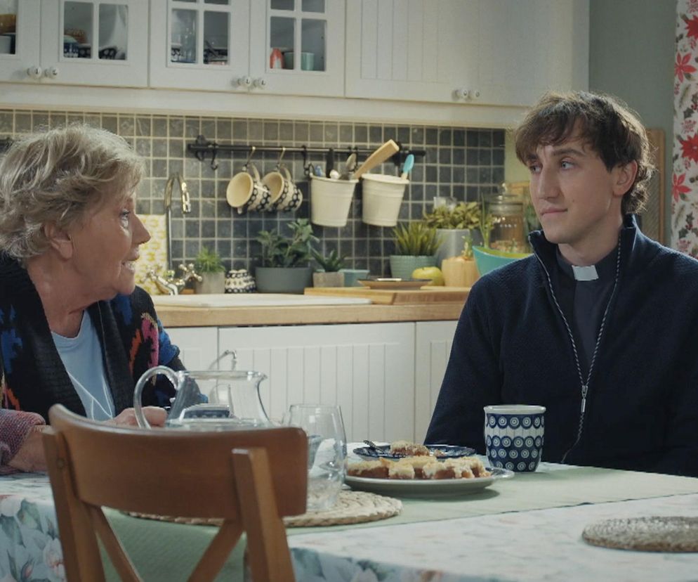 Barbara (Teresa Lipowska) rozmawia z księdzem Grzegorzem (Paweł Janyst) w kuchni, prosząc o wsparcie po stracie Franki. Barbara siedzi z lewej strony, ksiądz Grzegorz z prawej. Na stole leży ciasto i kubek z niebieskim wzorem. Więcej o ich losach na Super Seriale.