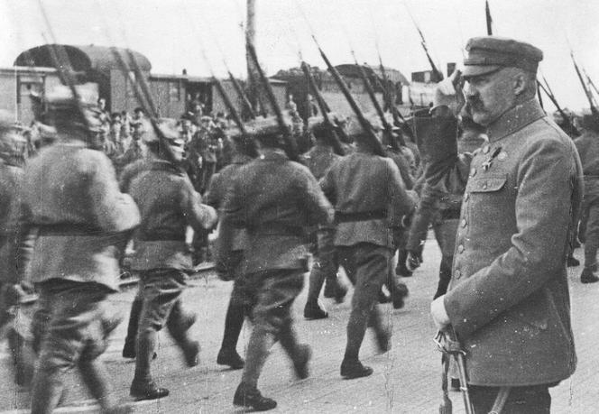 Naczelnik Państwa Józef Piłsudski odbiera defiladę oddziału piechoty na dworcu kolejowym. Na jego mundurze widać krzyż Virtuti Militari i znak oficerski „Parasol”.