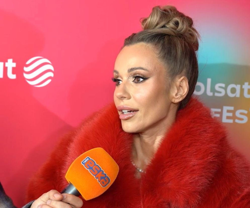 Wokalistka Doda w intensywnym makijażu i rudym futerku, z włosami upiętymi w kok, rozmawia z dziennikarzem Radia Eska. Artykuł na Poradnik Zdrowie dotyczy tego, ile waży Doda i dlaczego celowo przytyła.