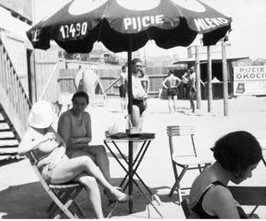 Plażowicze podczas wypoczynku pod parasolem z napisem Pijcie mleko. W tle widoczna rekalma z napisem Pikcie piwo Okocimskie. Zdjęcie zrobione w 1931 roku 