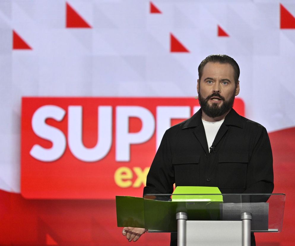 Krzysztof Stanowski przy pulpicie na tle logo Super Express. O jego wykształceniu i karierze przeczytasz na SE.