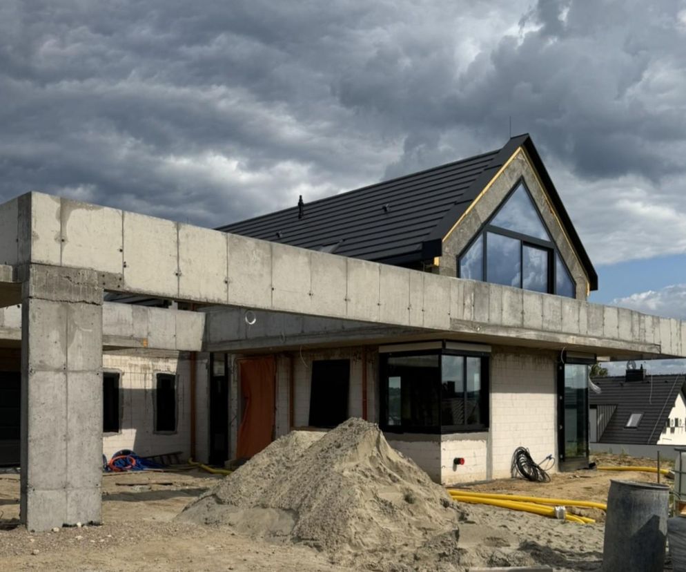 Budynek mieszkalny jednorodzinny w Wieliczce autorstwa KJ Architekci S.C. w trakcie budowy. Widoczne elementy konstrukcji żelbetowej, białe ściany parteru, antracytowy dach oraz duże przeszklenia na piętrze. Więcej o projekcie na Architektura Murator Plus.