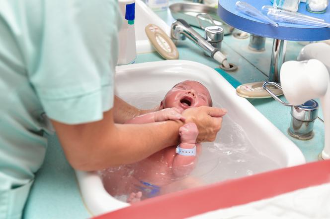 Noworodek kąpany przez położną w szpitalnej umywalce