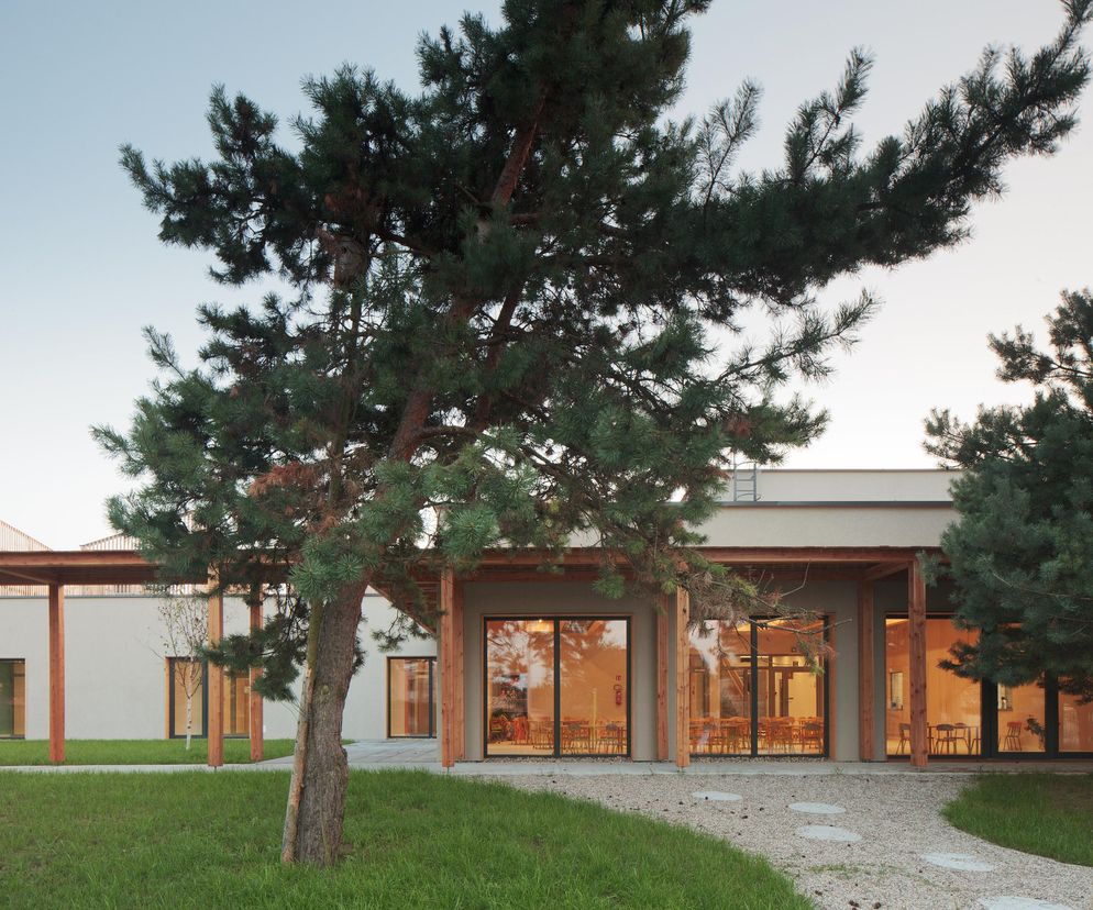 Przedszkole i żłobek w Jemielnicy autorstwa CH+ architekci, z drewnianą pergolą oraz dużymi oknami ukazującymi wnętrze z dziecięcymi meblami. Obiekt, zgłoszony do konkursu Życie w Architekturze 2025, stanowi ważny przykład dobrej praktyki w projektowaniu architektury dla dzieci na łamach Architektura Murator Plus.