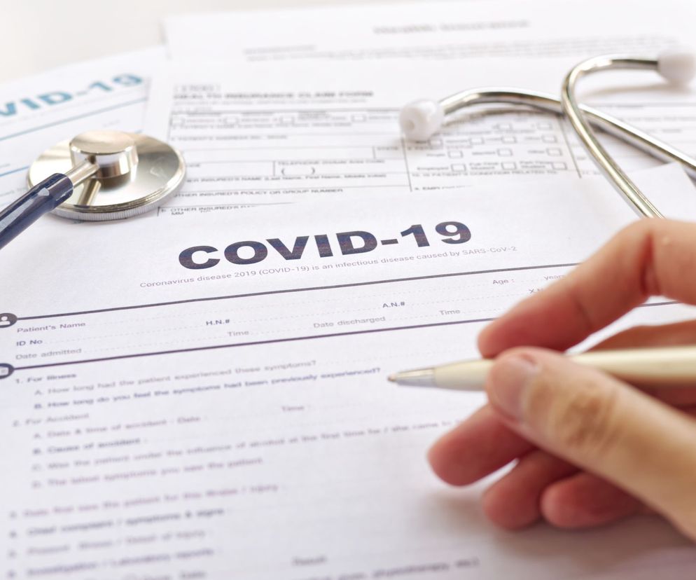 Ręka osoby wypełniającej formularz medyczny z nagłówkiem „COVID-19”, obok leży stetoskop. Terapia osoczem ozdrowieńców, jej zalety oraz jak oddać osocze po COVID-19, przeczytasz na portalu Poradnik Zdrowie.