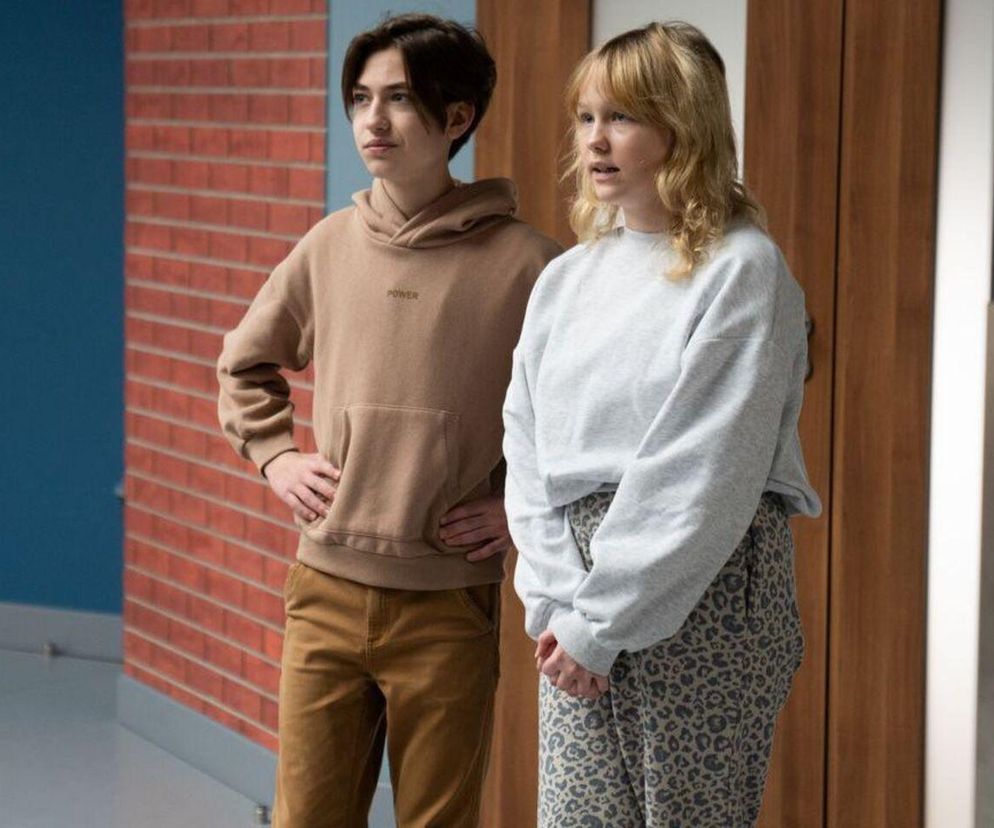 Emilka (Jessica Frankiewicz) i Emil (Artem Malaszczuk) w luźnych strojach, stojący w korytarzu, z ceglaną ścianą w tle. Nastolatkowie wydają się zaniepokojeni, co sugeruje napiętą atmosferę w serialu Barwy szczęścia. Więcej o losach bohaterów przeczytasz na Super Seriale.