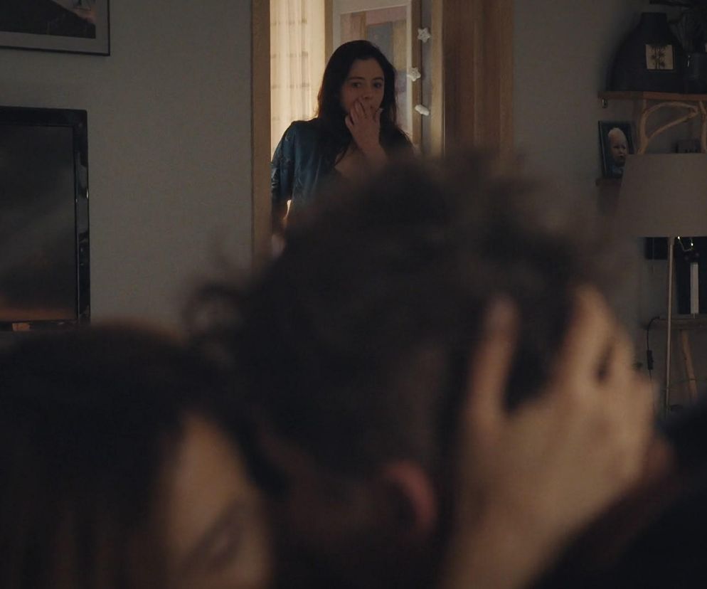 Iza zaskoczona spogląda z progu, widząc Kamę i Marcina na kanapie, pogrążonych w intymnej rozmowie. Zdjęcie ukazuje początek dziwnego trójkąta w M jak miłość, o którym więcej przeczytasz na Super Seriale.