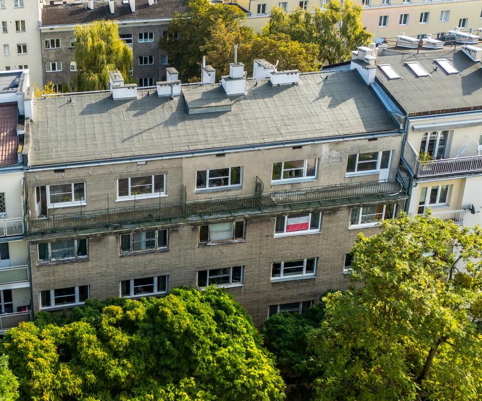 Widok z lotu ptaka na kamienicę Jerzego Wierzbickiego przy Alei Niepodległości w Warszawie, z elewacją z cegły cementowej, płaskim dachem z kominami i świetlikami. Poniżej widać bujne korony drzew. O historii i architekturze tego miejsca przeczytasz na Architektura Murator Plus.