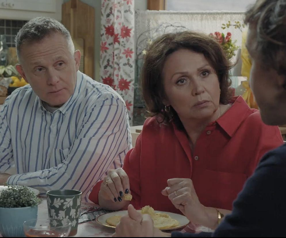 Paweł Janyst jako Ksiądz Grzegorz, Teresa Lipowska jako Barbara Mostowiak oraz Małgorzata Pieńkowska jako Marysia Rogowska siedzą przy stole w kuchni. Ksiądz Grzegorz, w koszuli w paski, patrzy z powagą, Marysia w czerwonej koszuli trzyma kawałek jedzenia, a Barbara Mostowiak słucha. Mostowiakowie dowiadują się o nadchodzących problemach w Grabinie. Więcej o ich losach na Super Seriale.