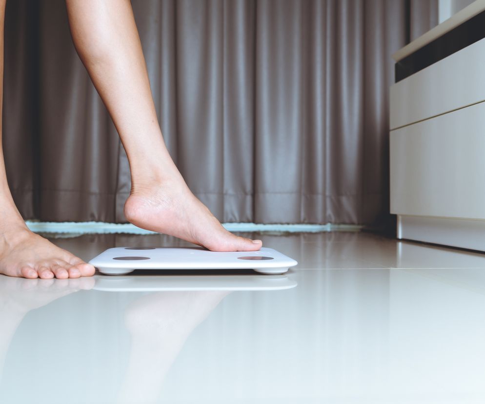 Kobieta stoi na wadze w sypialni. 