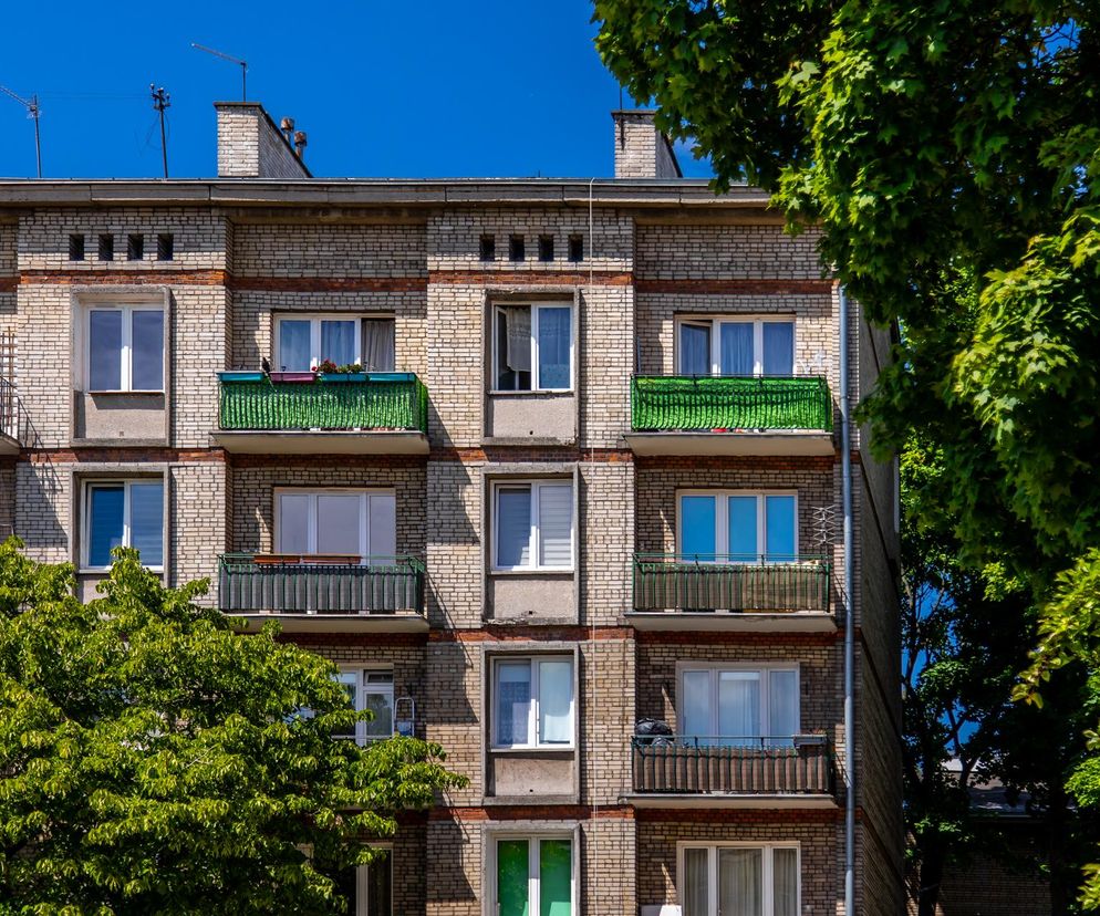 Stary blok mieszkalny z cegły na warszawskich Bielanach symbolizuje zaniedbane oszczędności z PRL. Balkony z metalowymi barierkami, okna z roletami i anteny na dachu ukazują realia dawnych lat. Temat waloryzacji książeczek mieszkaniowych jest poruszany na Super Biznes.