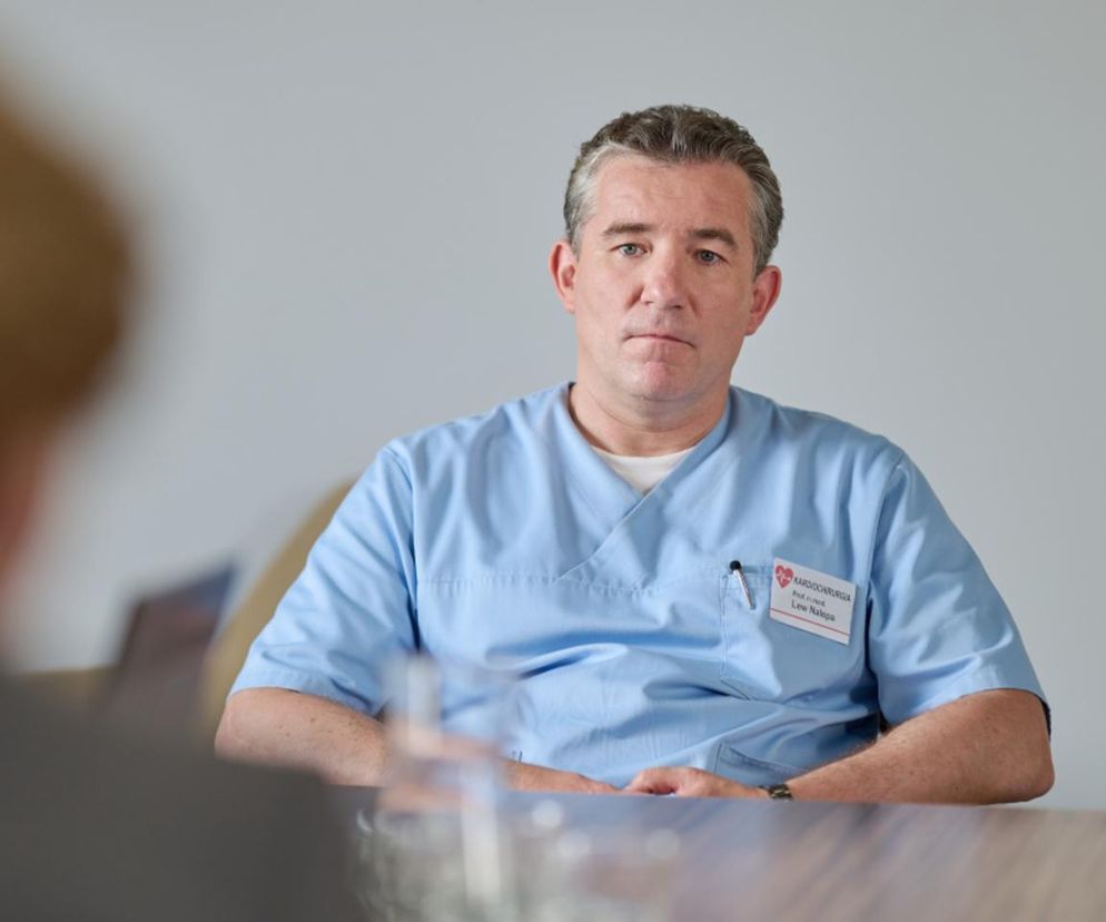 Lew Nalepa w lekarskim stroju, z poważną miną, siedzi przy stole. Lekarz trzyma ręce złożone. Na identyfikatorze widnieje napis Kardiochirurgia, Prof. dr hab. med. Lew Nalepa. Ta postać to kluczowy bohater odcinków, o których przeczytasz na Super Seriale.