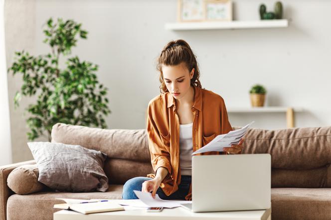 Młoda kobieta zajmująca się przeglądaniem papierów podczasy pracy przy komputerze