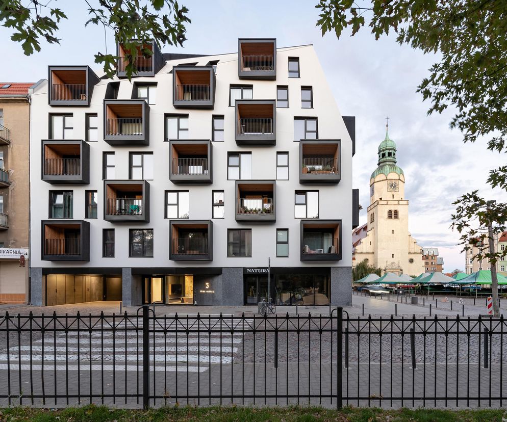 Nowoczesna kamienica autorstwa Ultra architects z asymetrycznymi, wysuniętymi balkonami, na tle historycznej zabudowy Poznania i wieży kościoła pw. Maryi Królowej. Projekt prezentowany na Architektura Murator Plus to przykład innowacyjnej architektury miejskiej.