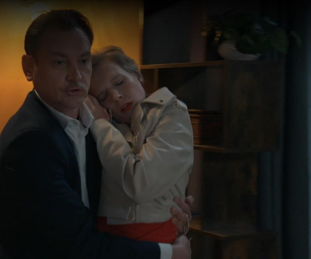 Robert Stefaniak (Paweł Ławrynowicz) podtrzymuje nieprzytomną Sonię (Weronika Nockowska) w odcinku 3240 serialu Barwy szczęścia. Mężczyzna w ciemnej marynarce i białej koszuli, z wąsami, obejmuje bladą kobietę w jasnej kurtce i czerwonej bluzce, która ma zamknięte oczy i opiera głowę na jego ramieniu. Więcej informacji o serialu Barwy szczęścia znajdziesz na Super Seriale.