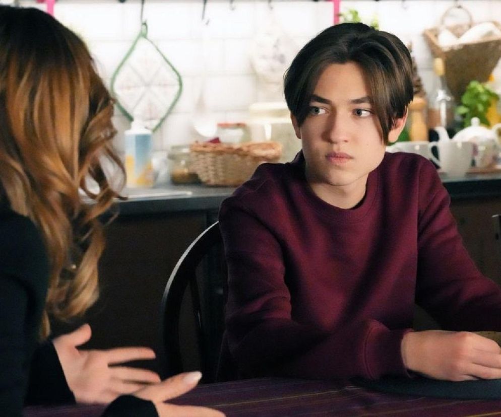 Emil (Artem Malashchuk) w bordowej bluzie siedzi przy stole z zawiedzioną Asią (Anna Gzyra) w czarnej bluzce i kręconych włosach, dyskutując o planach wakacyjnych w 3282. odcinku Barw szczęścia. Więcej o serialu przeczytasz na Super Seriale.