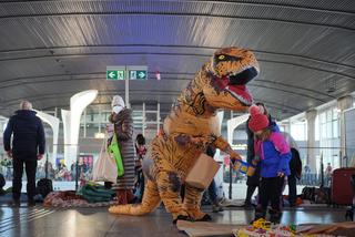 Dinozaur na Dworcu Centralnym - mieszkaniec Warszawy wywołuje uśmiech na twarzach małych uchodźców