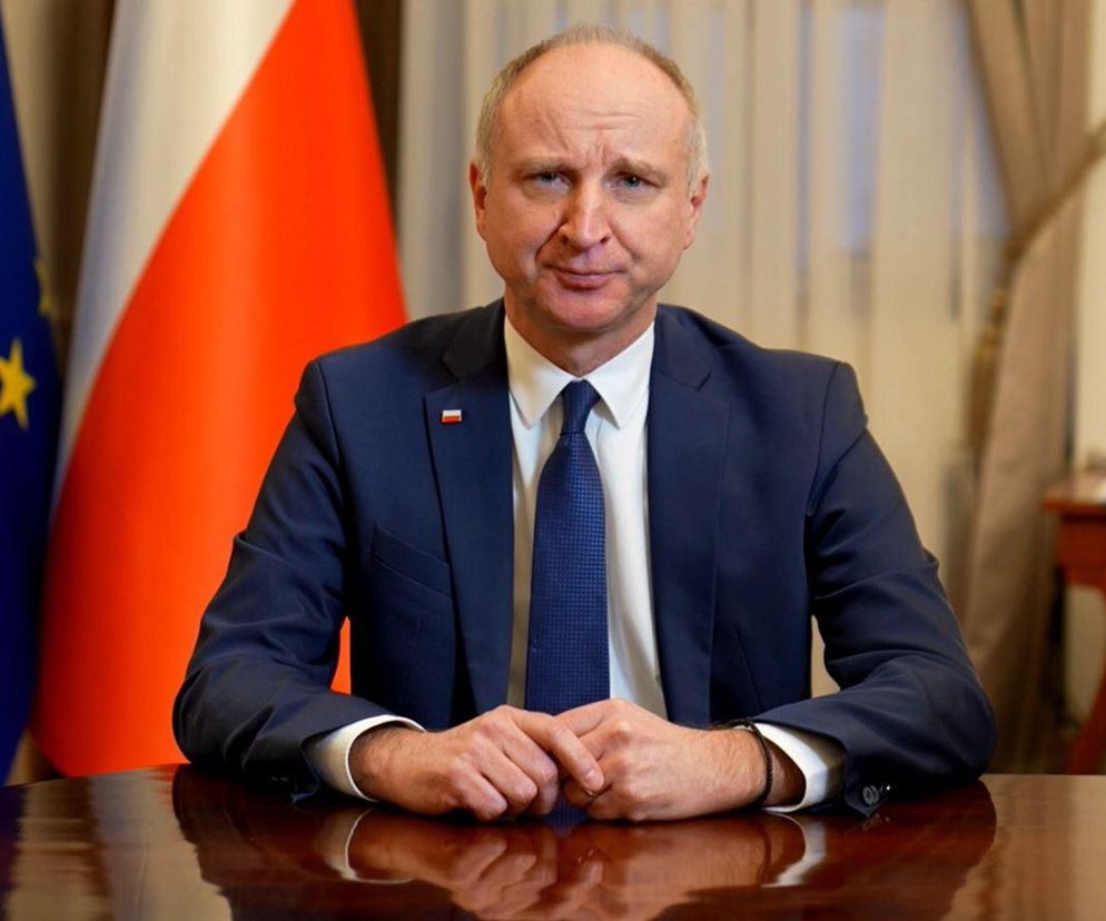 Wojciech Kolarski na tle flag Polski i UE. O znaczeniu polityki historycznej przeczytasz na SE Polityka.