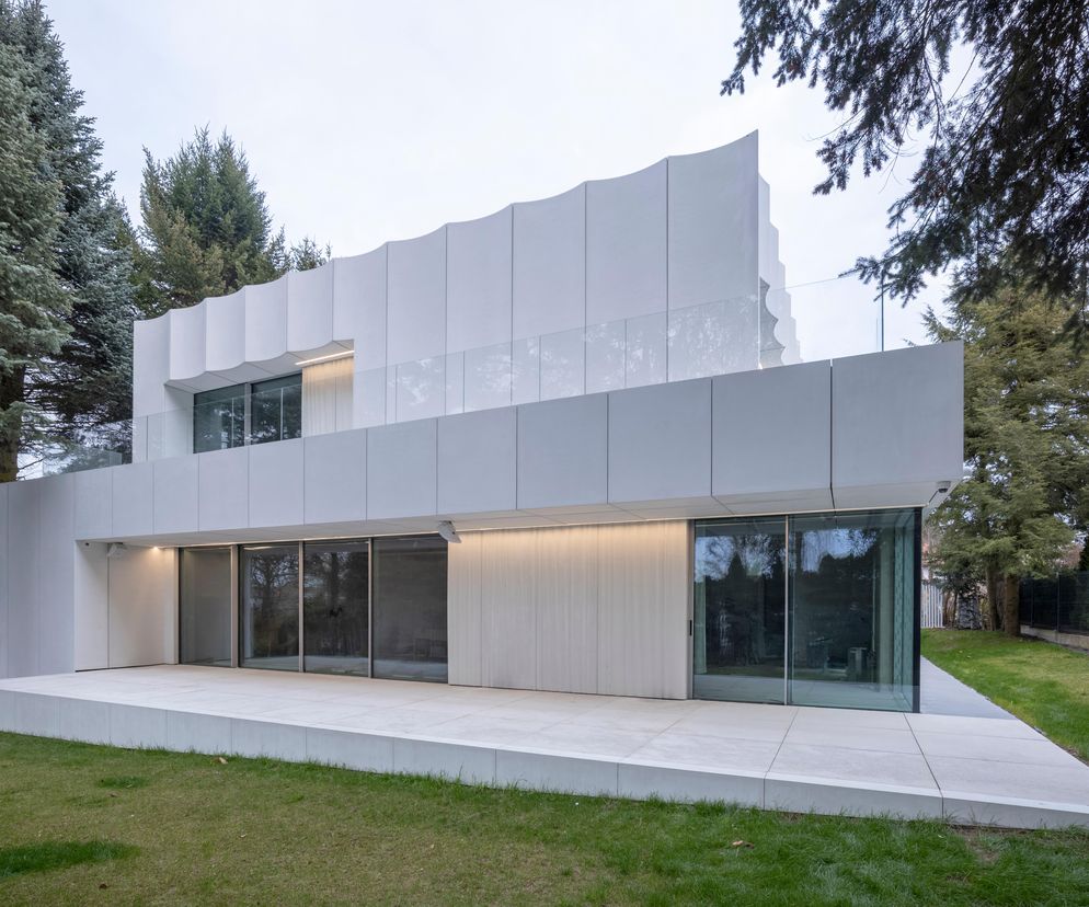 Dom Biały w Krakowie, projekt architektów Marka Szpindy i Piotra Uherka, to nowoczesna willa z płaskim dachem i białymi elewacjami z płyt GRC, otoczona zielenią. Obiekt, zgłoszony do konkursu Życie w Architekturze 2025, cechuje minimalistyczny styl i precyzyjne detale, o czym więcej można przeczytać na Architektura Murator Plus.