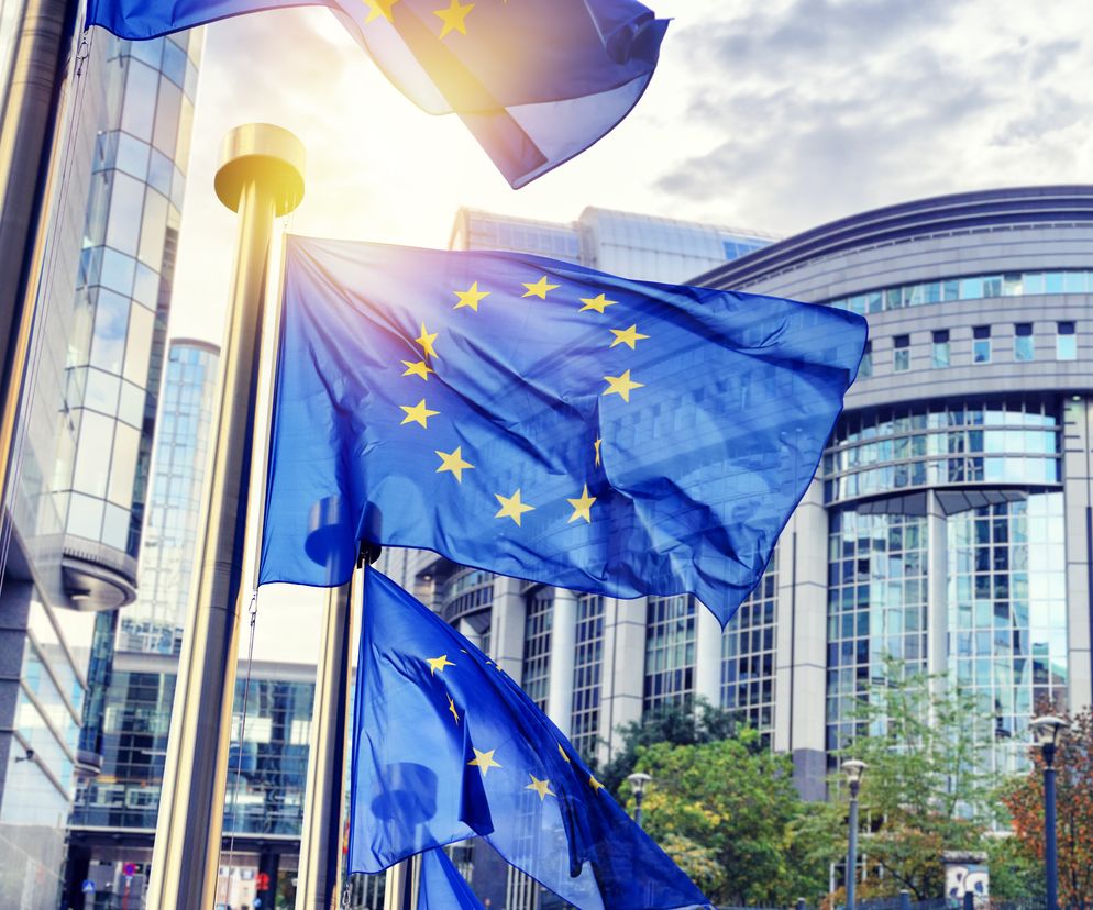 Flagi Unii Europejskiej powiewające na tle budynków Parlamentu Europejskiego w słoneczny dzień, symbolizujące decyzje UE dotyczące systemu ETS2, o których możesz przeczytać na Super Biznes.