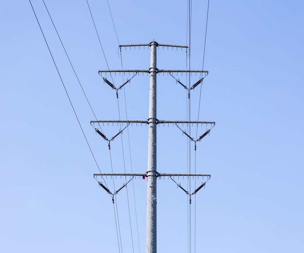 Metalowy słup energetyczny z wieloma liniami wysokiego napięcia na tle błękitnego nieba. Infrastruktura przesyłowa, która może stać na działce. Dowiedz się, jak uzyskać odszkodowanie za słup energetyczny, czytając artykuł na Super Biznes.
